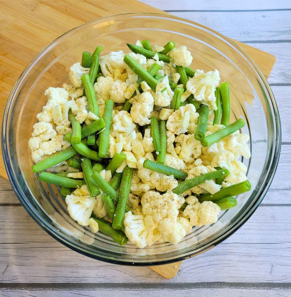 A bowl of fresh cut green beans, cauliflower florets, and garlic.