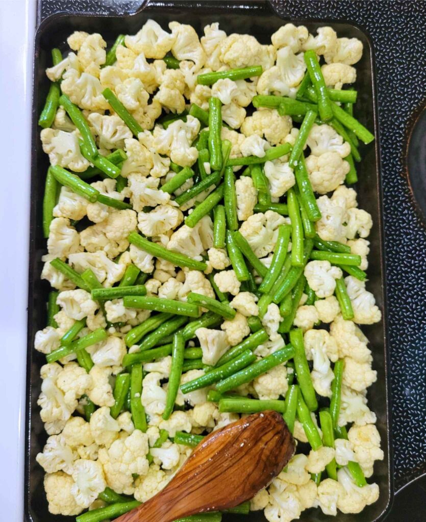 Fresh cut green beans, garlic, and cauliflower florets, coated in olive oil and spread out on a cast iron baking sheet