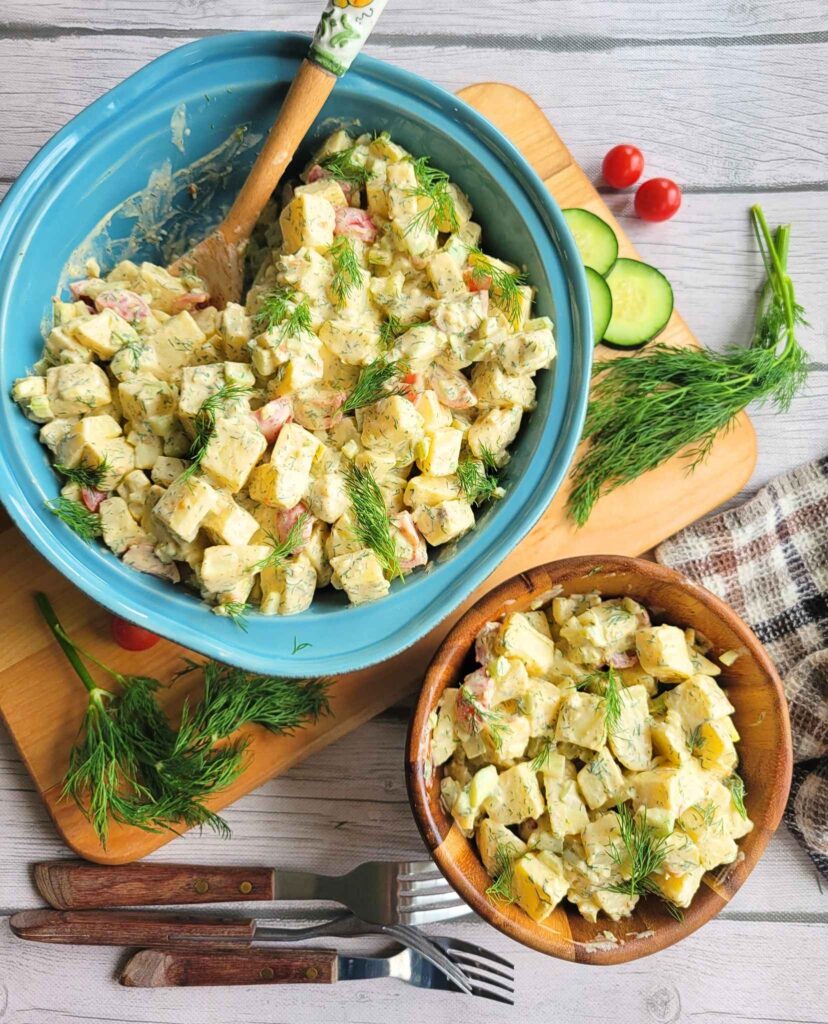 A serving dish and bowl of Classic sweet potato salad  with fresh dill, cucumber slices and cherry tomatoes.