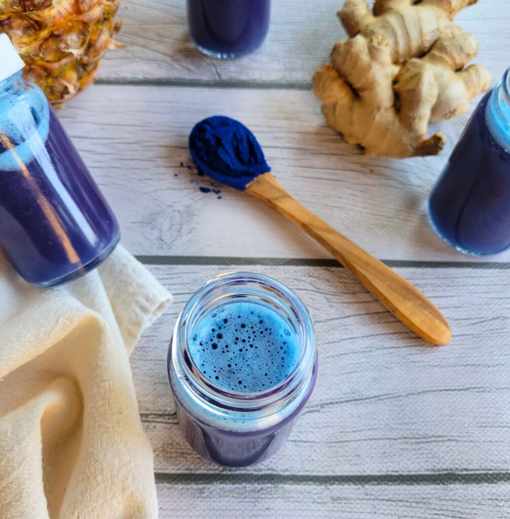 Blue wellness shots and fresh ginger root with a spoonful of vibrant blue powder