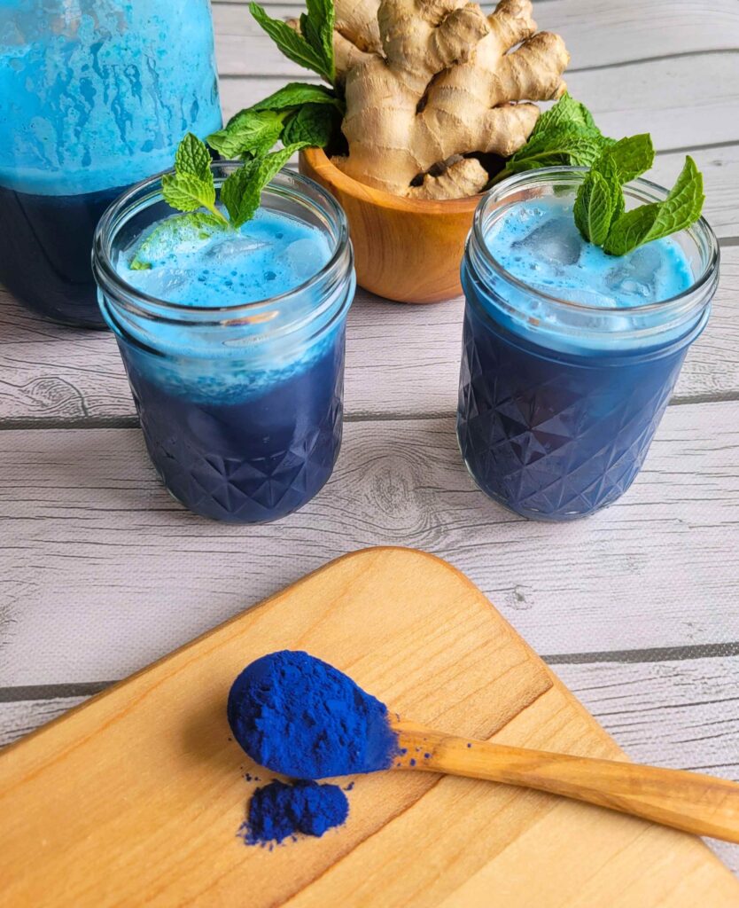 A spoonful of Blue spirulina powder next to healing anti-inflammatory juice with fresh mint and ginger