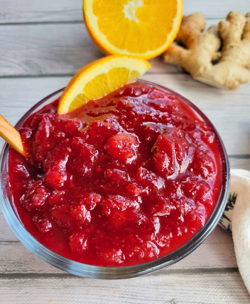 a bowl of homemade healthy cranberry sauce with fresh ginger and refined sugar-free garnished with an orange slice