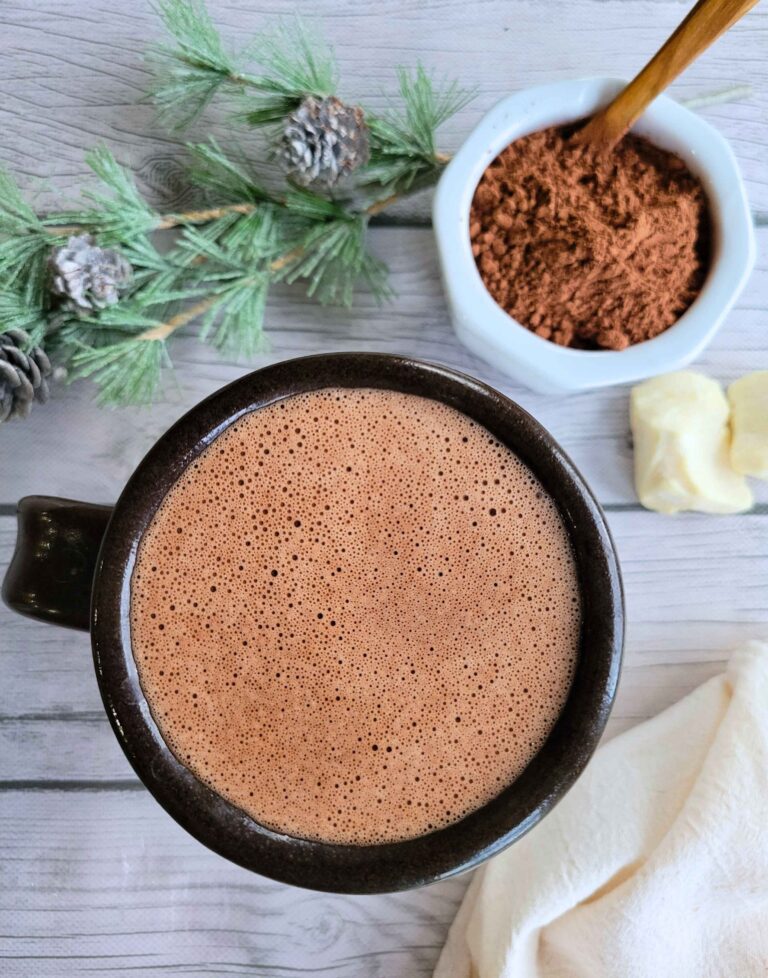 A cup of gut-healing bone broth hot chocolate with a bowl of raw cacao powder and fresh cacao butter