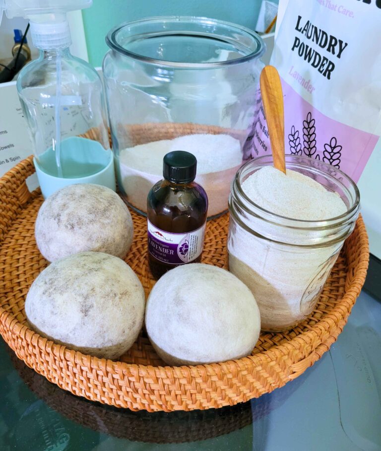 Display of simple non-toxic laundry routine products: natural laundry powder, essential oil, wool dryer balls in a basket