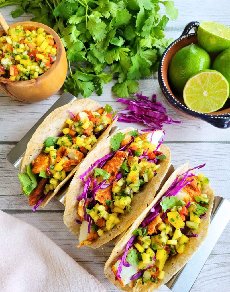 baked anti-inflammatory fish tacos on gut-healthy buckwheat tortillas topped with fresh mango salsa, purple cabbage, cilantro and limes