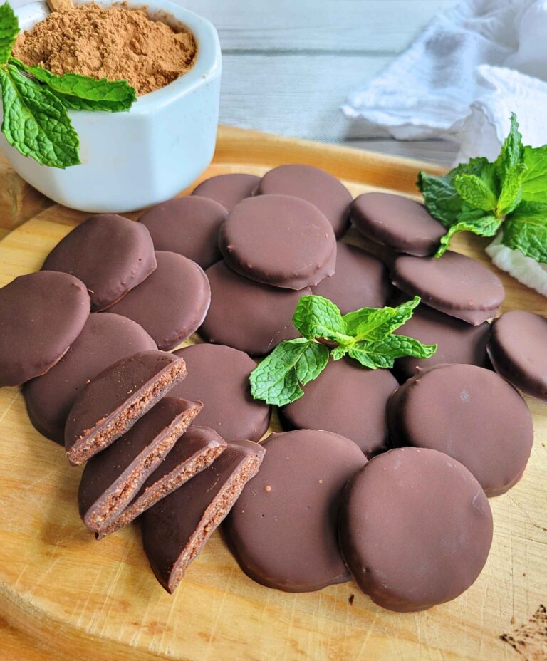 Fresh homemade gluten-free thin mints next to a bowl of cacao and fresh mint leaves, a refined sugar-free treat.